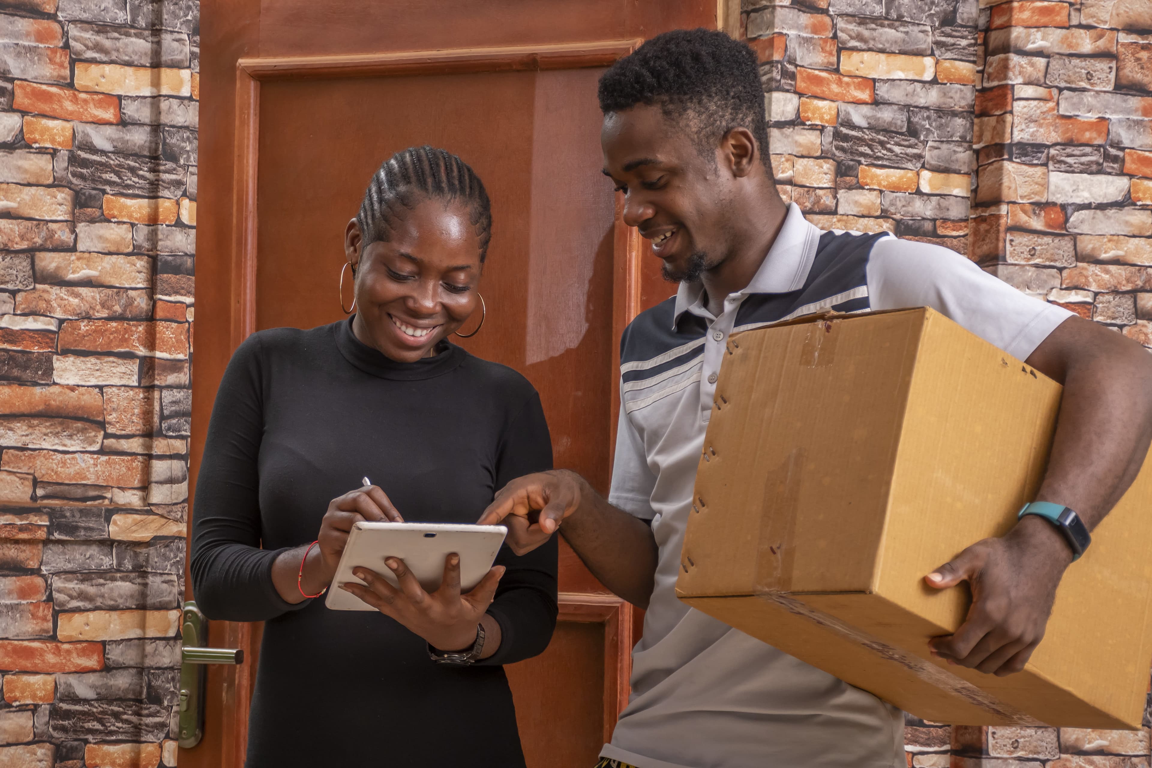 African couple at their doorstep, woman signing for package delivery